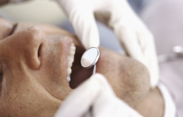 Dentist inspecting man's teeth with angled mirror, close-up