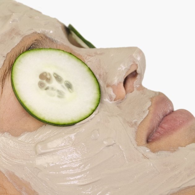 Young woman with mud mask and cucumber slices on eyes