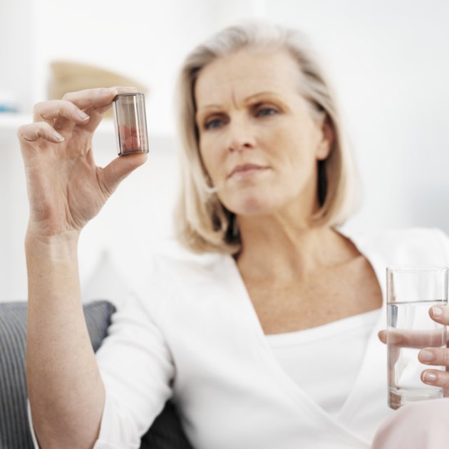 Mature woman on sofa, holding pills and glass of water (focus on foreground)