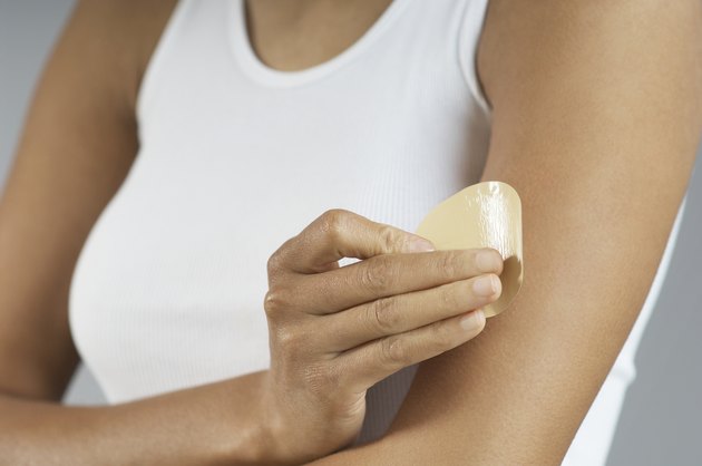 Woman applying patch to arm, mid section