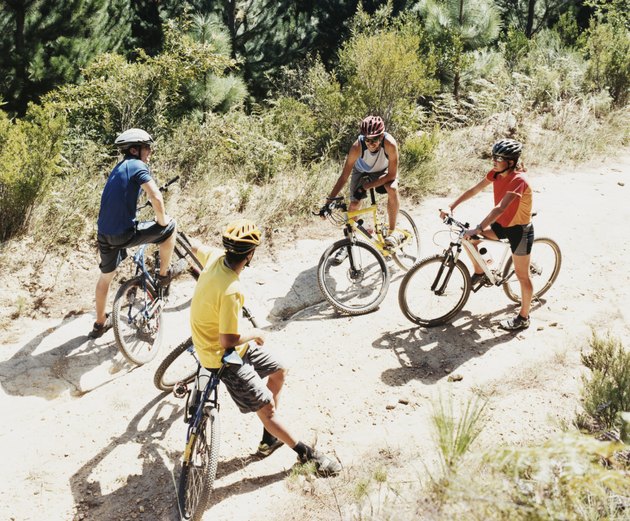 Four People Chatting on a Dirt Road in a Forest Riding Mountain Bikes