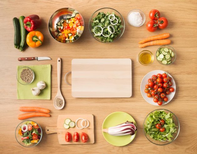 Creative vegetarian cooking at home concept with fresh healthy vegetables chopped, salads and kitchen wooden utensils, top view with copy space