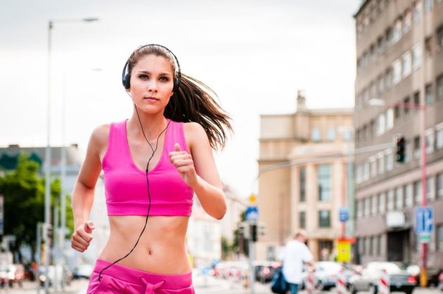 Young beautiful woman with headphones jogging and listening music in street