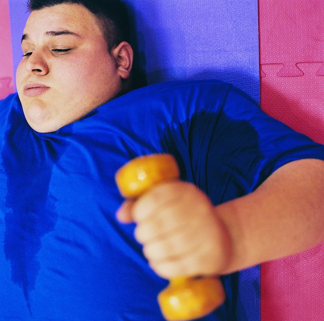 Young Man Lying on an Exercise Mat Lifting a Dumbbell
