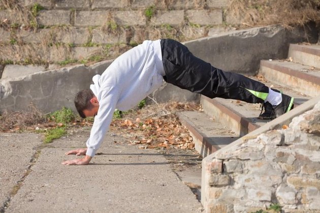 Attractive young man is exercising outdoors. He is doing push-ups on the staircase.