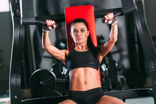 caucasian woman exercising on shoulder press machine in gym