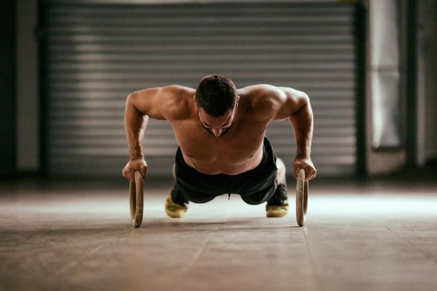 Young stron man is doing push-ups by rings.