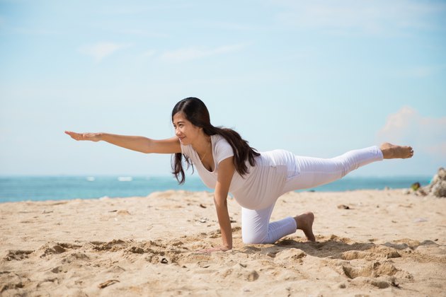 Pregnant asian woman doing yoga in the sea shore
