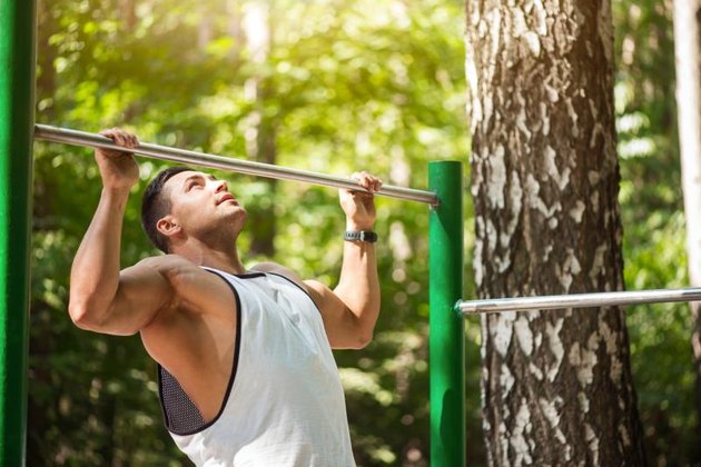 Building up strength. Handsome hard working confident man holding a horizontal bar and doing chin ups while working out