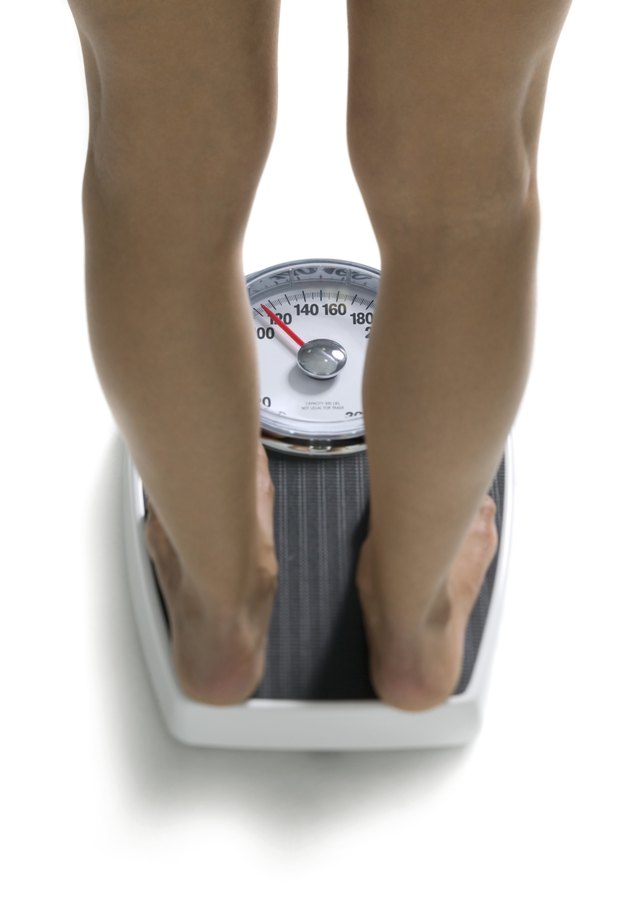conceptual shot of the legs of a young adult woman as she stands on a bathroom scale