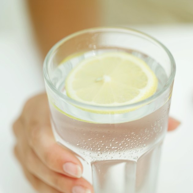 Close-up of a woman's hand holding a glass of water with a lemon wedge