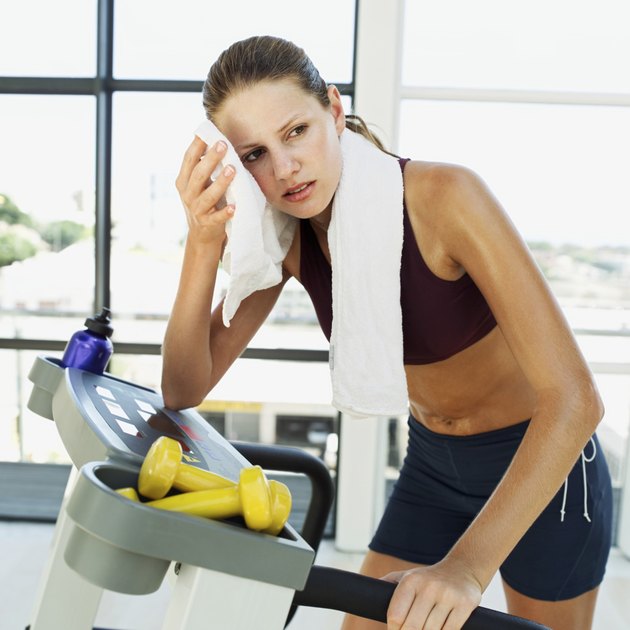 woman standing on a treadmill and wiping her face