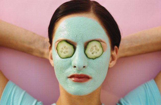 woman lying down with a face pack and cucumber slices