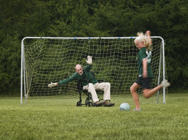 Girl (10-11) playing soccer with grandfather in wheelchair as goal keeper