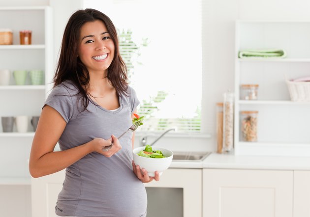 Attractive pregnant woman holding a bowl of salad while standing
