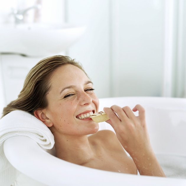 portrait of a young woman in a bathtub eating a snacking and smiling