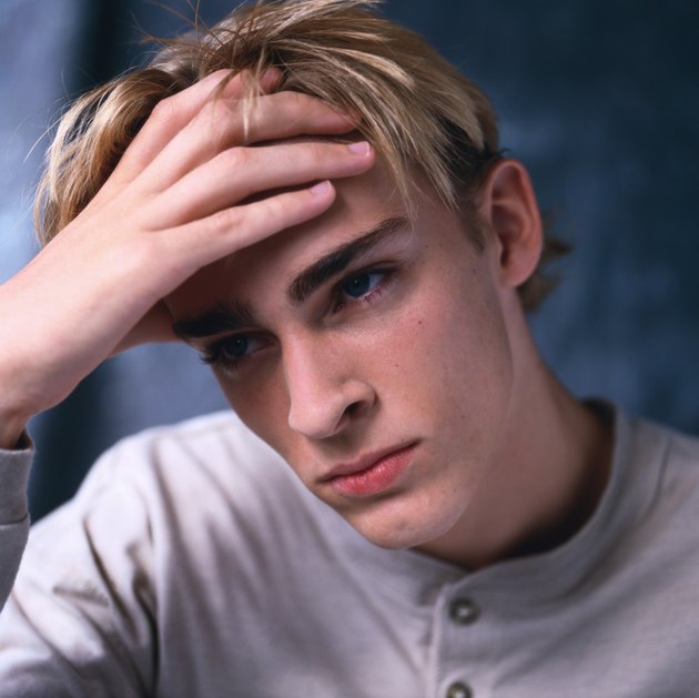 close-up of depressed young boy holding his forehead in his hand
