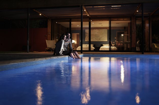 Young couple sitting at edge of pool at night
