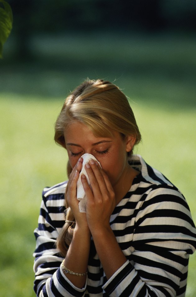 Young woman blowing nose, eyes closed, outdoors