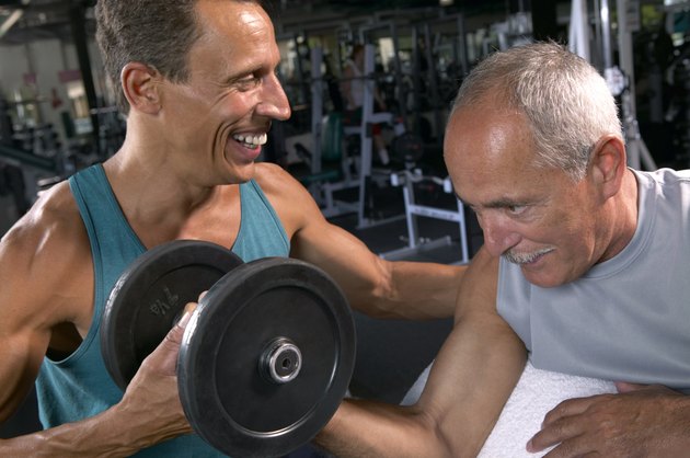 Two mature men in gym, one lifting weights