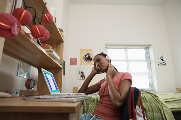 Young woman sitting at desk, wearing headphones, in student dormitory