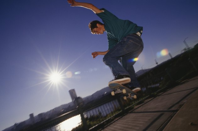 Teenage boy (16-17) performing tricks with skateboard on sidewalk, low angle view