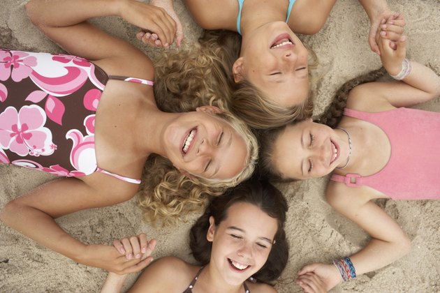 Four girls (8-12) lying in circle on beach, holding hands, eyes closed