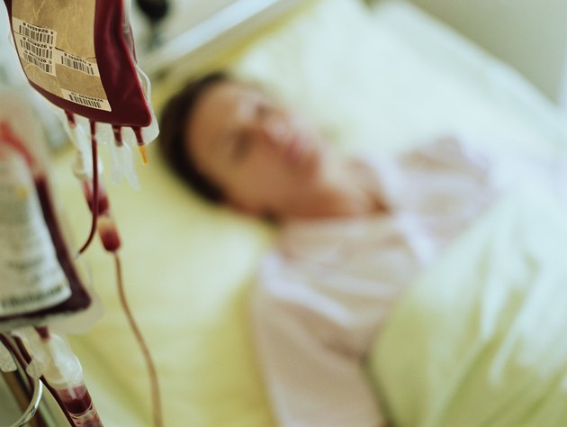Woman in hospital bed by IV drip filled with blood (focus on drip)