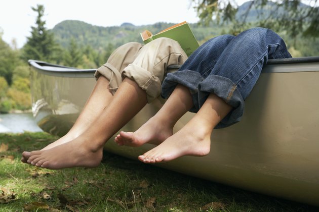 Barefoot boy and girl (4-10 years) reading in canoe by lake, low section