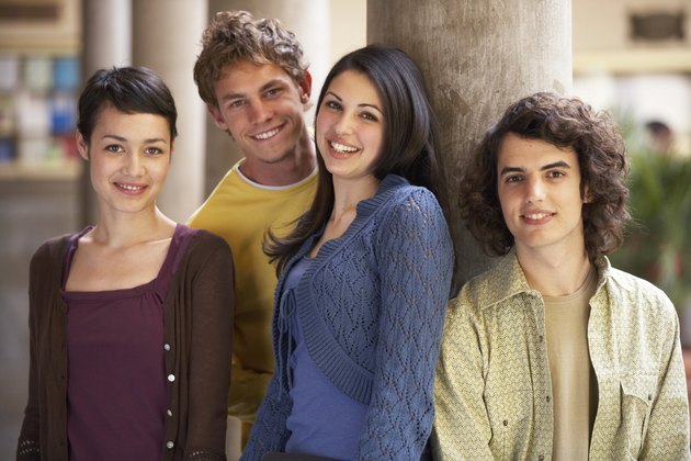 Four young men and women standing by column, smiling, portrait