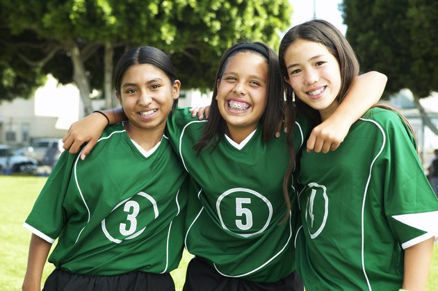 Female footballers (11-13) standing arm in arm, smiling, portrait