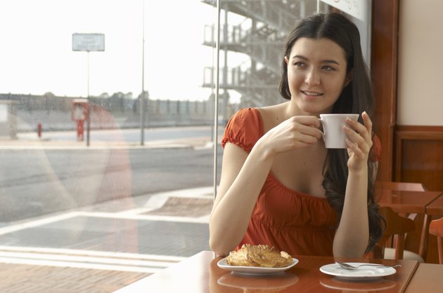 Young woman in cafe holding coffee cup smiling, portrait