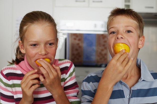 Twin brother and sister (10-12) with oranges in mouths, close-up