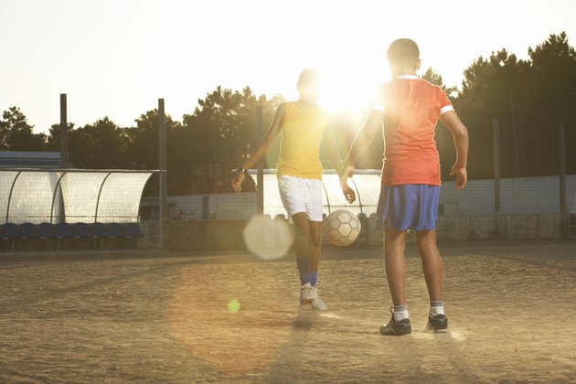Two boys (11-13) playing football, lens flare