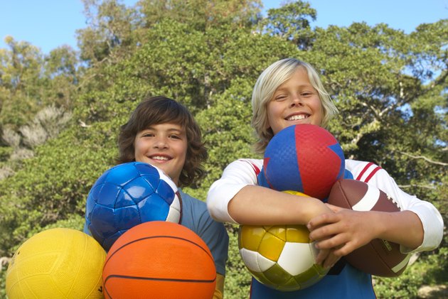Two boys (11-13) holding sport balls outdoors, smiling, portrait, low angle view
