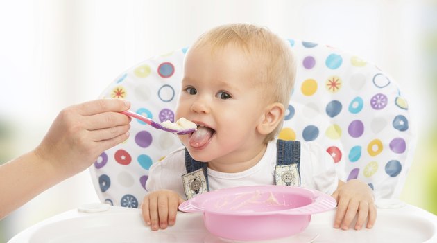 happy mother feeds funny baby from spoon