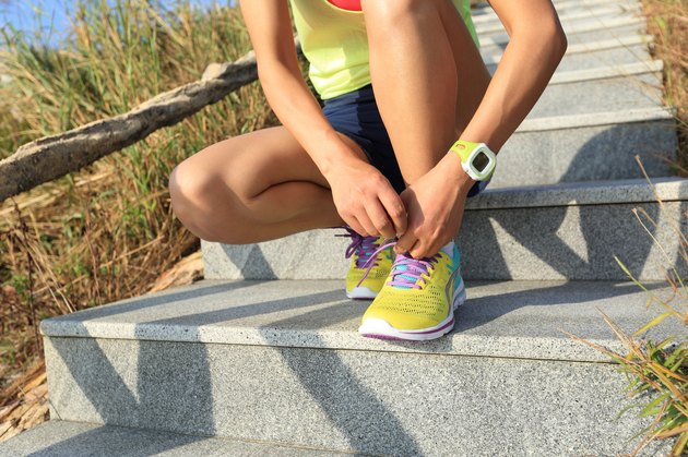 young woman runner tying shoelaces on stone trail