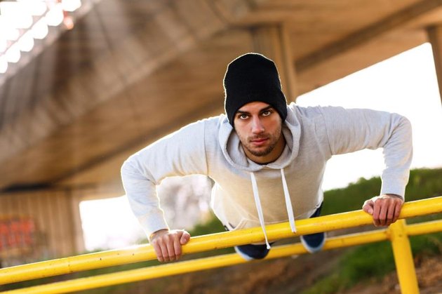 Young man doing push ups on the handrail under the bridge.