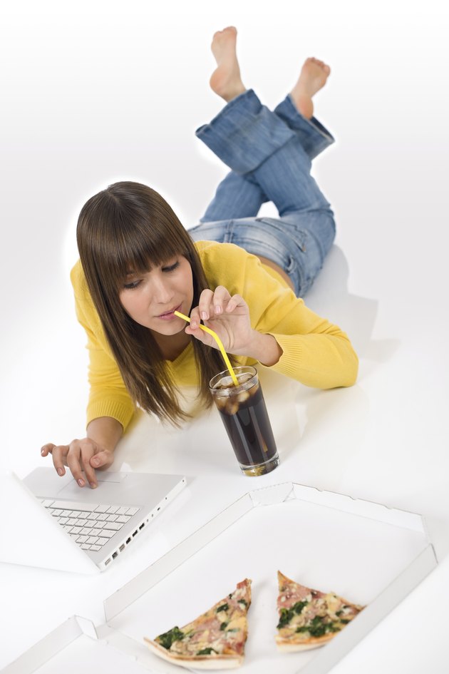 Happy female teenager with laptop lying down drink cola