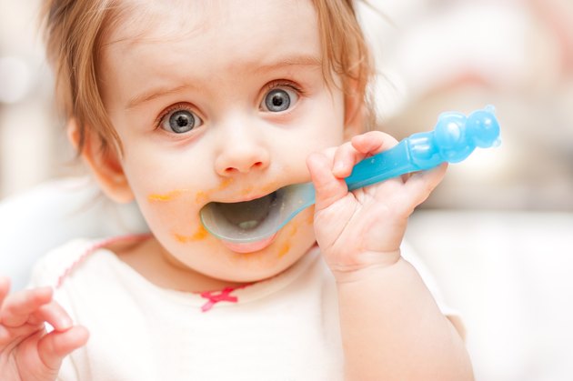 little girl feeding from a spoon on blue chair.