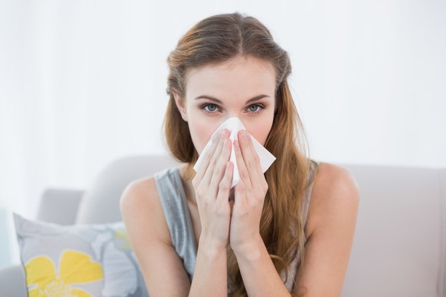 Sick young woman sitting on sofa blowing her nose