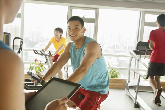 Young man on stationary bike exercising with his personal trainer