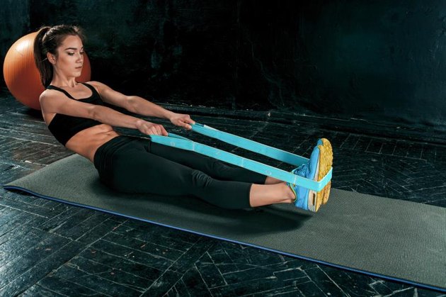 The brunette athletic woman exercising with rubber tape on black wooden floor