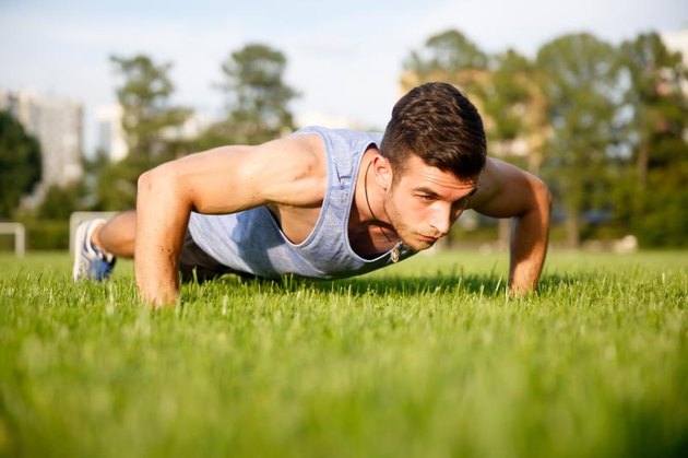 Handsome young man training in park and doing push-ups on green grass