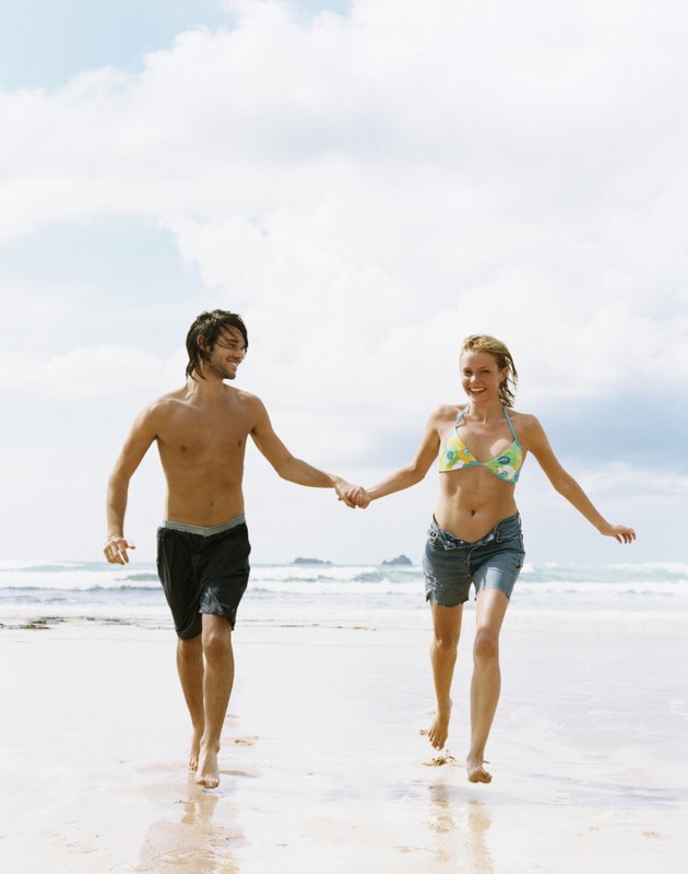 Young Couple in Swimwear Run on the Beach Holding Hands