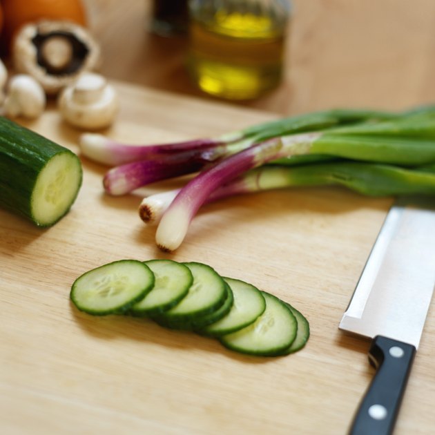 Close up of cucumber slices and onions and mushrooms and a knife lying on a chopping board
