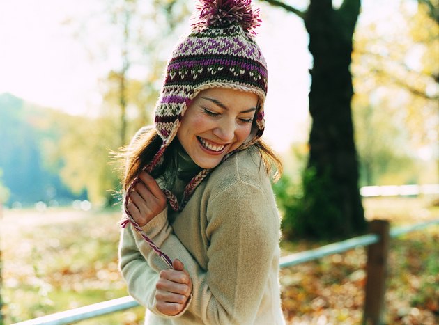 Portrait of a Young Woman Wearing a Bobble Hat Smiling With Her Arms in Front and Her Eyes Closed