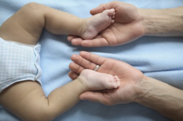 Close-up of a person's hands holding a baby's legs