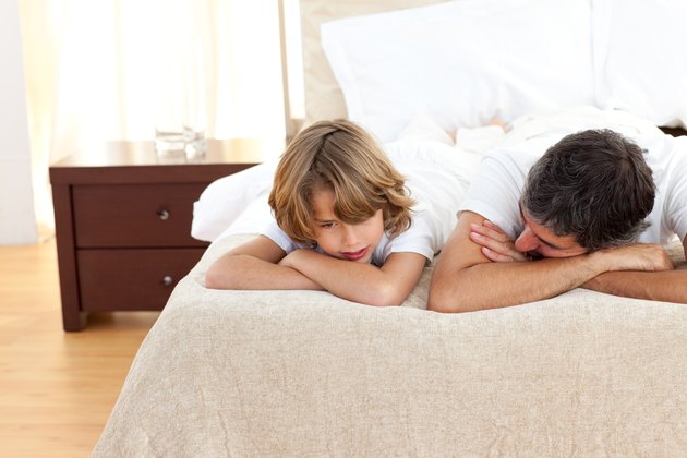 Earing father talking with his son lying on bed