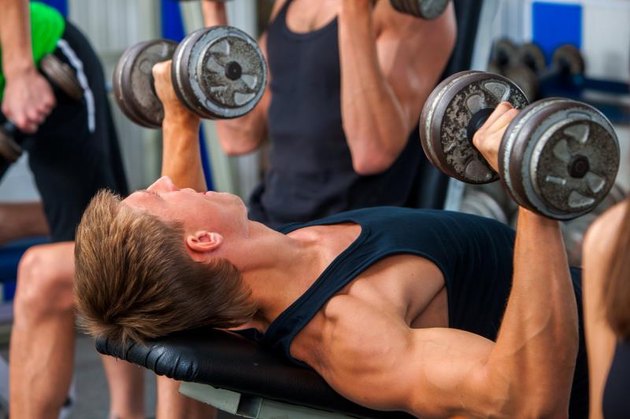 Group of men working on simulator his body at gym. Man with big biceps on foreground in sport gym.